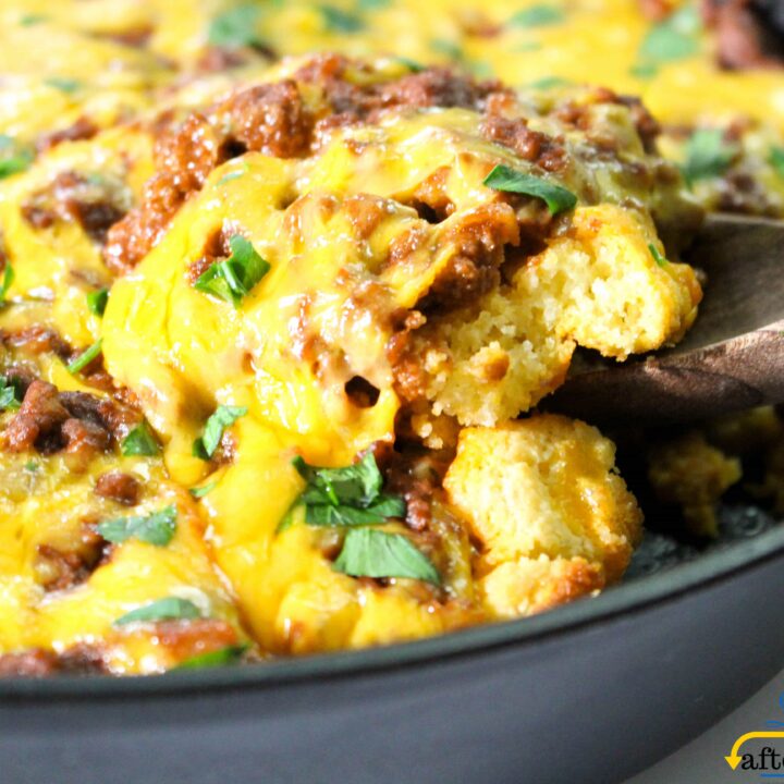 a black cast iron skillet with layers of cornbread, ground beef, and cheese