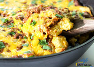 a black cast iron skillet with layers of cornbread, ground beef, and cheese