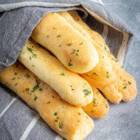 gluten free breadsticks stacked in a pyramid. They are sprinkled with parsley and wrapped in a towel.