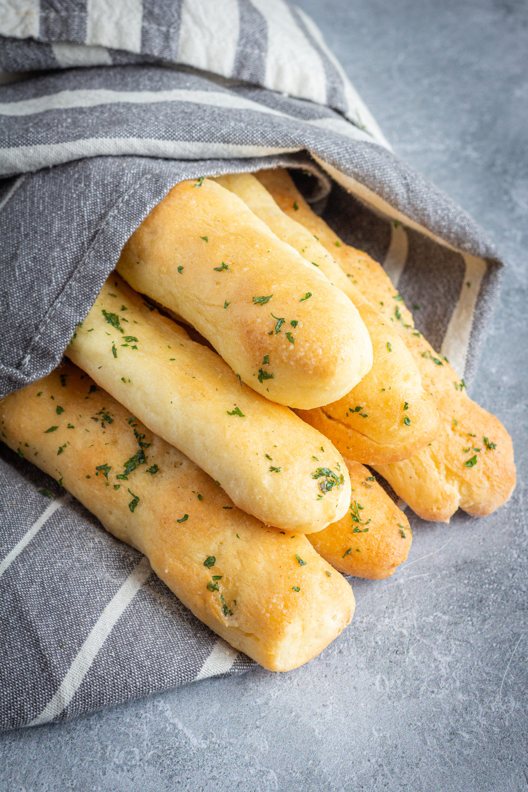 gluten free breadsticks stacked in a pyramid. They are sprinkled with parsley and wrapped in a towel.