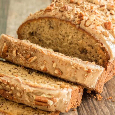 a loaf of gluten free banana bread partially sliced. It has a light brown glaze and chopped pecans on top