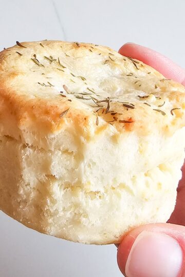 hand holding a tall, flaky biscuit