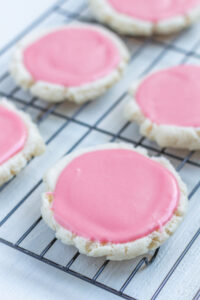 Round sugar cookies with pink frosting on a cooling rack.