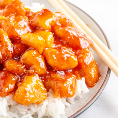 a speckled plate with rice topped with orange-glazed chunks of chicken and chopsticks on the side