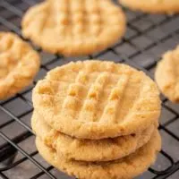 A stack of 3 round peanut butter cookies sit on a cooling rack.