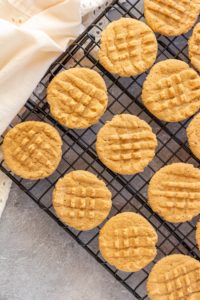 Round peanut butter cookies sit on a cooling rack over a gray backdrop.