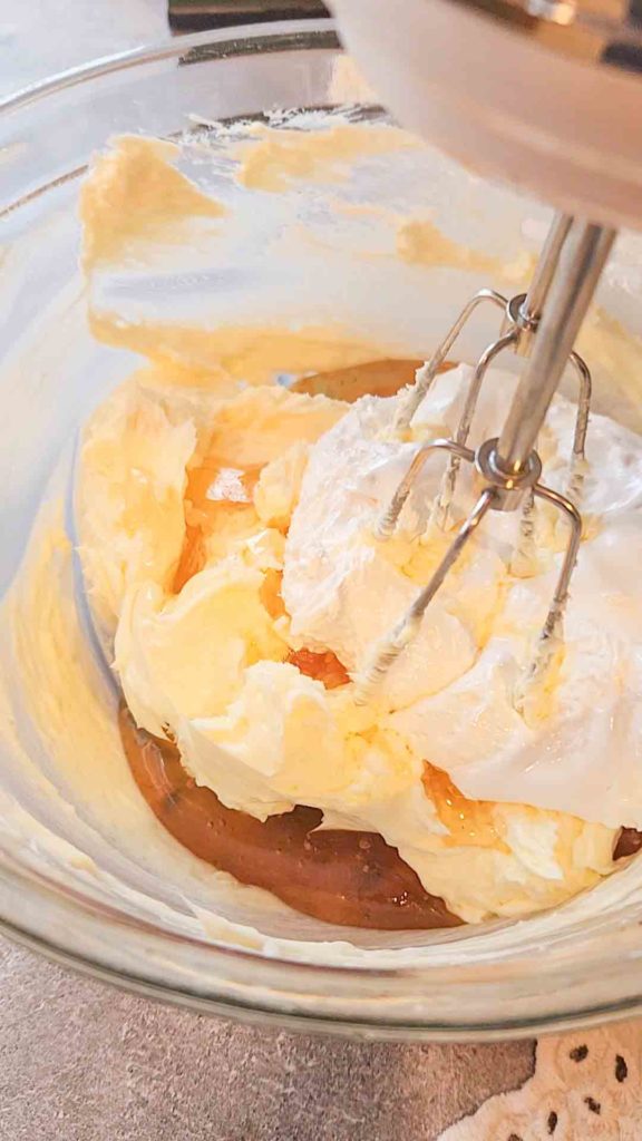 A hand mixer sits in a glass bowl filled with butter, honey, and marshmallow cream.