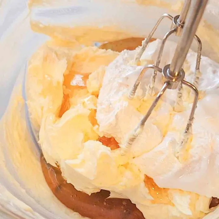 A hand mixer sits in a glass bowl filled with butter, honey, and marshmallow cream.