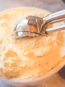 A cookie scoop is scooping honey butter out of a white bowl.