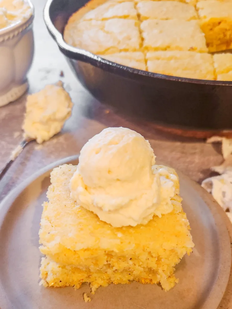 a dollop of honey butter is pictured on top of a square slice of cornbread.