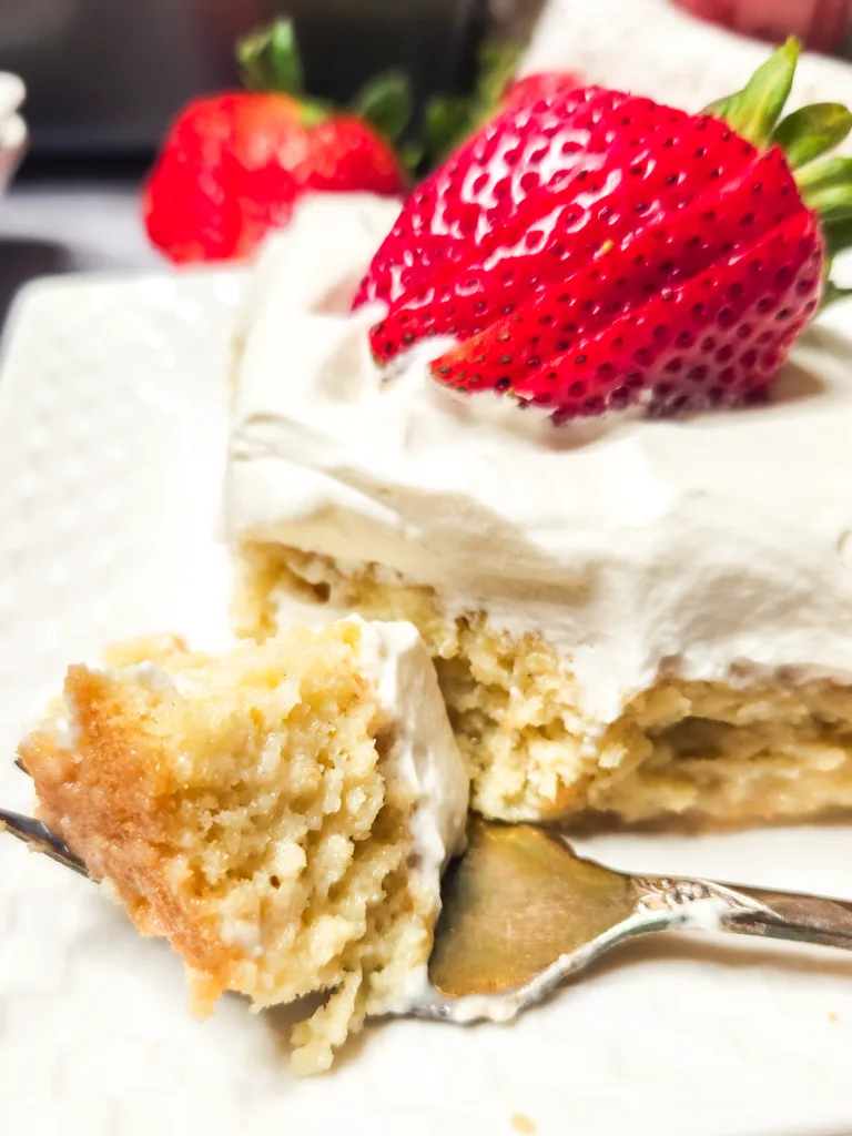 A slice of tres leches with a bite-sized piece on a fork. It looks soft and delicate without being soggy.