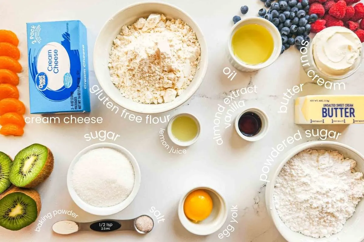 An image displaying ingredients in this recipe: cream cheese, gluten-free flour, lemon juice, sugar, baking powder, salt, egg yolk, almond extract, vanilla, oil, butter, sour cream, and powdered sugar