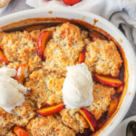 A white oval serving dish with caramely peaches and a golden biscuit topping.