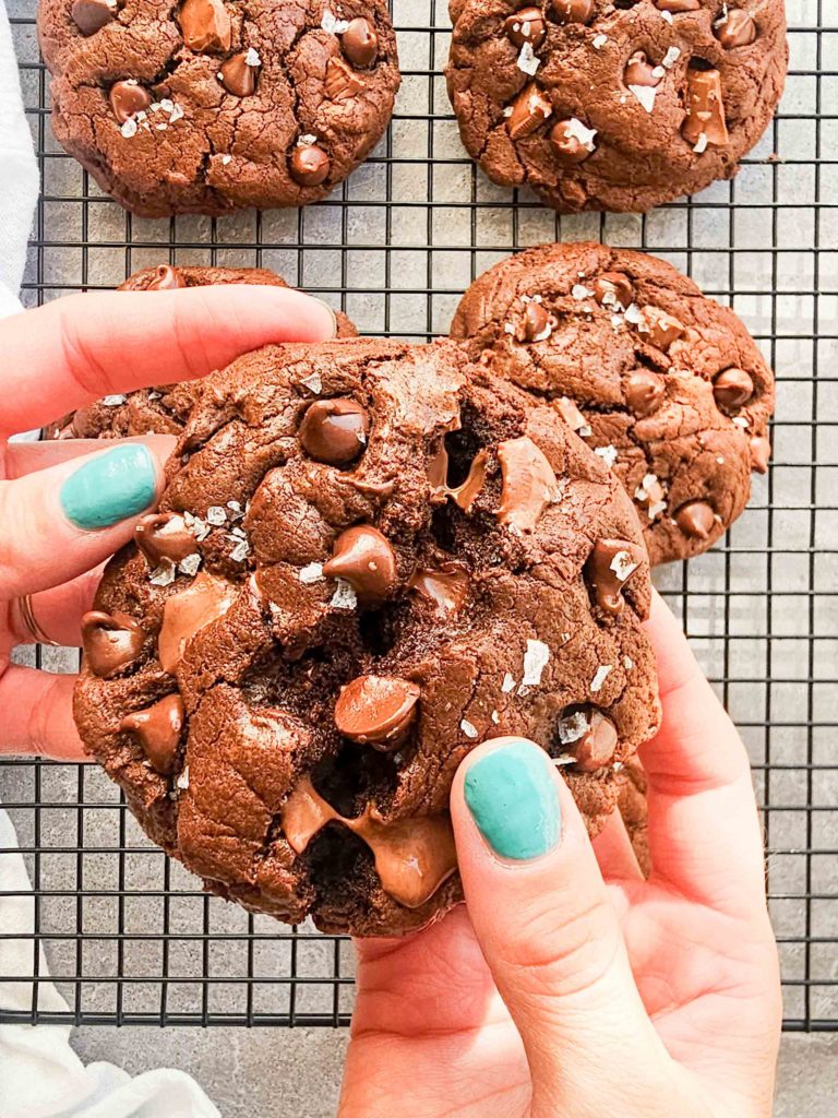 A hand breaks apart a cookie exposing a soft and fudgy interior and melty chocolate.