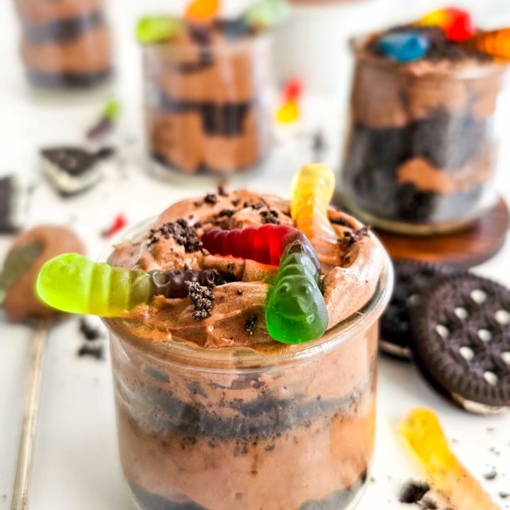 Chocolate pudding and Oreo cookie crumbs are layered in a small glass cup and topped with 3 colored gummy worms.