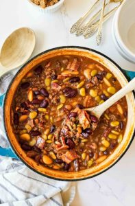 a dutch oven full of baked beans with bacon, ground beef, and a thick, dark sauce