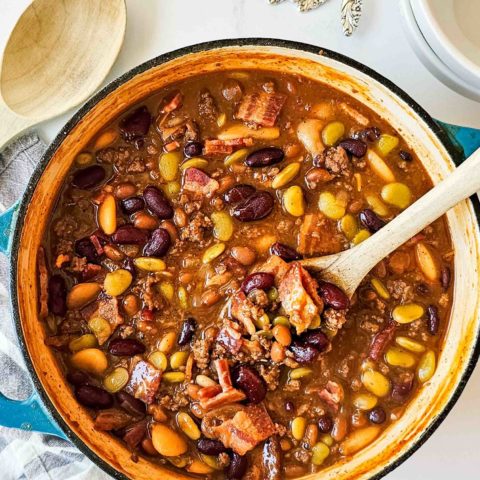 a dutch oven full of baked beans with bacon, ground beef, and a thick, dark sauce