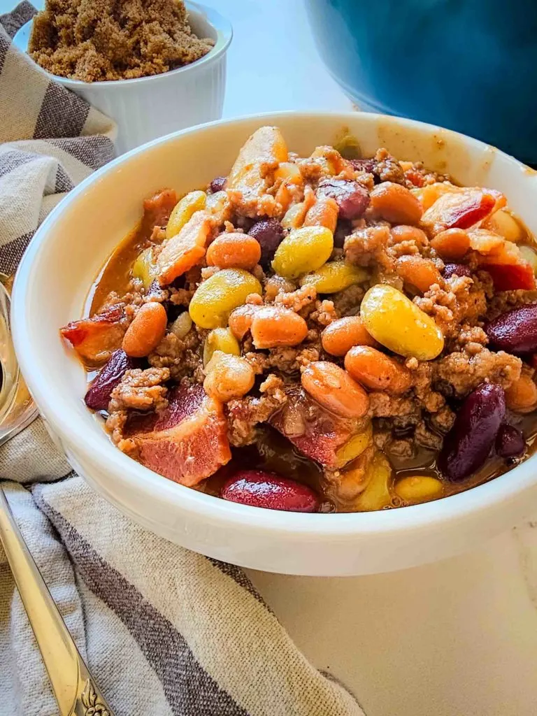 a bowl of southern baked beans. You can see different kinds of beans, strips of bacon, and chunks of ground beef.