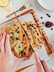 a hand slices a loaf of gluten free Irish soda bread speckled with raisins