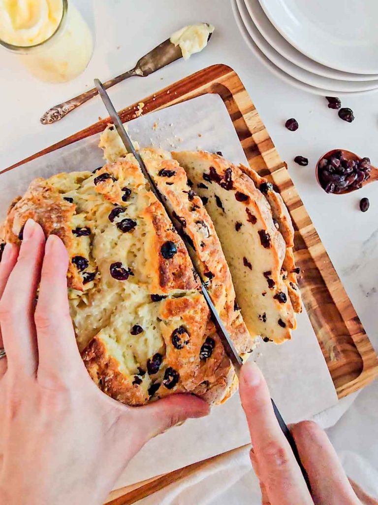 a hand slices a loaf of gluten free Irish soda bread speckled with raisins