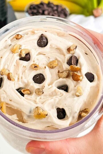hand holding a Ninja Creami pint container with banana ice cream. Topped with chocolate chips and walnuts