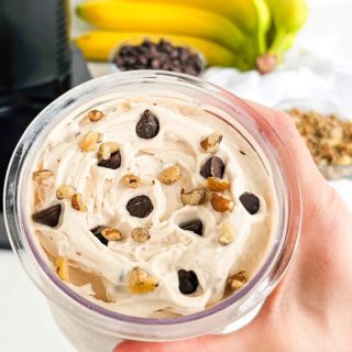 hand holding a Ninja Creami pint container with banana ice cream. Topped with chocolate chips and walnuts