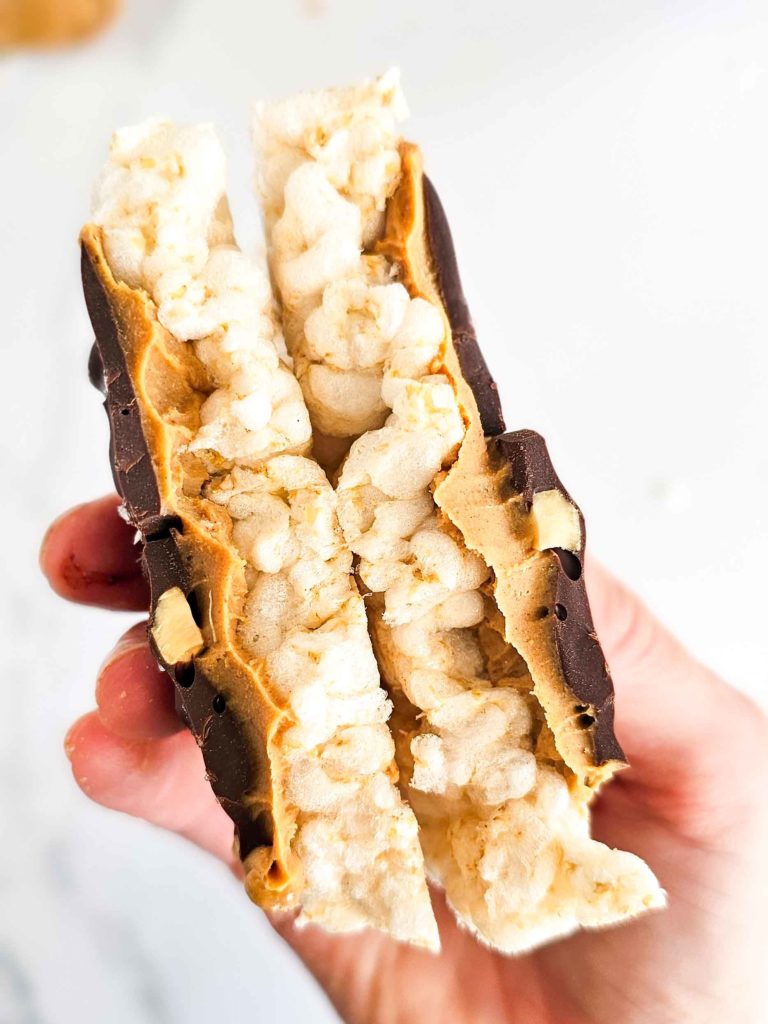 a hand holding a chocolate and peanut butter covered rice cake