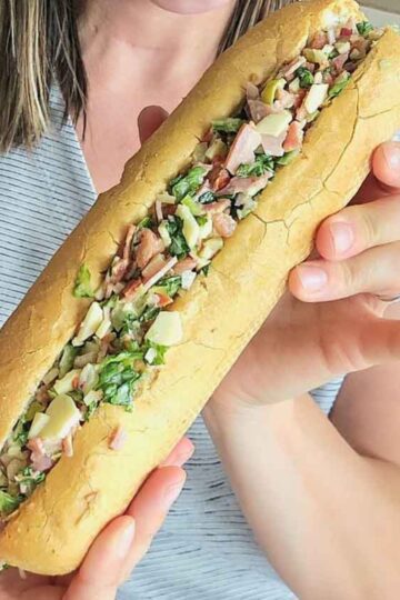 person holding a long sandwich stuffed with chopped meats and cheeses
