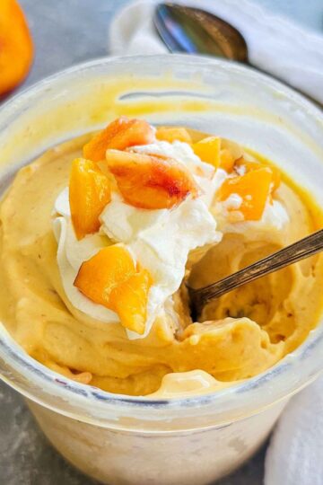 container of creamy peach ice cream with a spoon