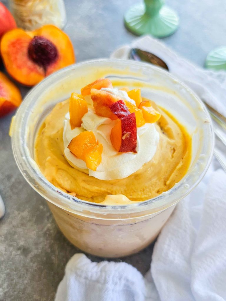 peach ice cream topped with whipped cream and fresh peaches