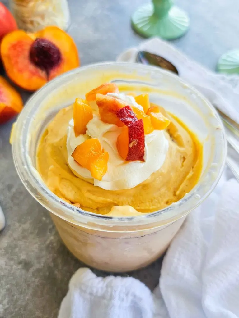 peach ice cream topped with whipped cream and fresh peaches